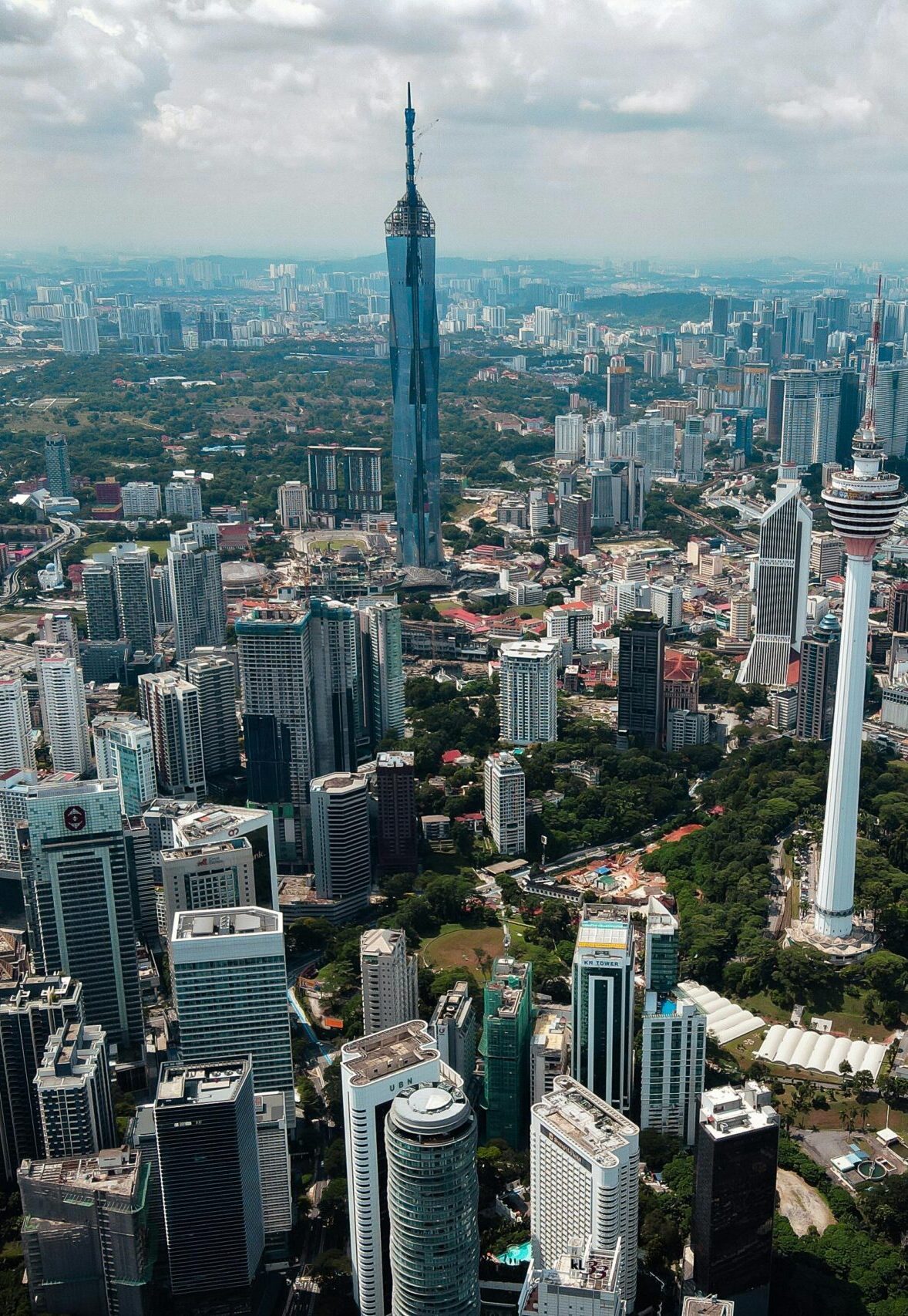 Stunning aerial view of Kuala Lumpur showcasing iconic skyscrapers and urban sprawl under a cloudy sky.
