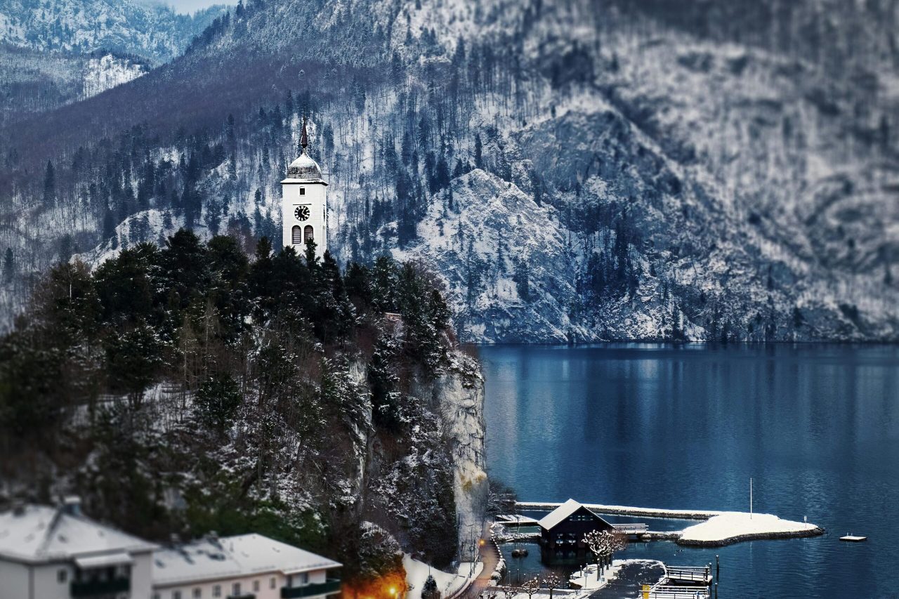 Scenic winter view of Traunkirchen in Austria with snowy mountains and a blue lake.
